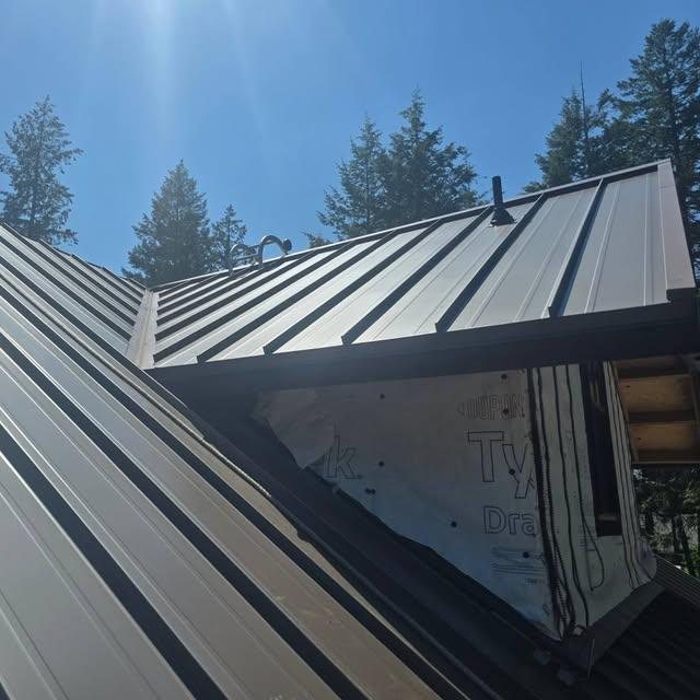 Standing seam metal panels meeting at a dormer against a blue sky
