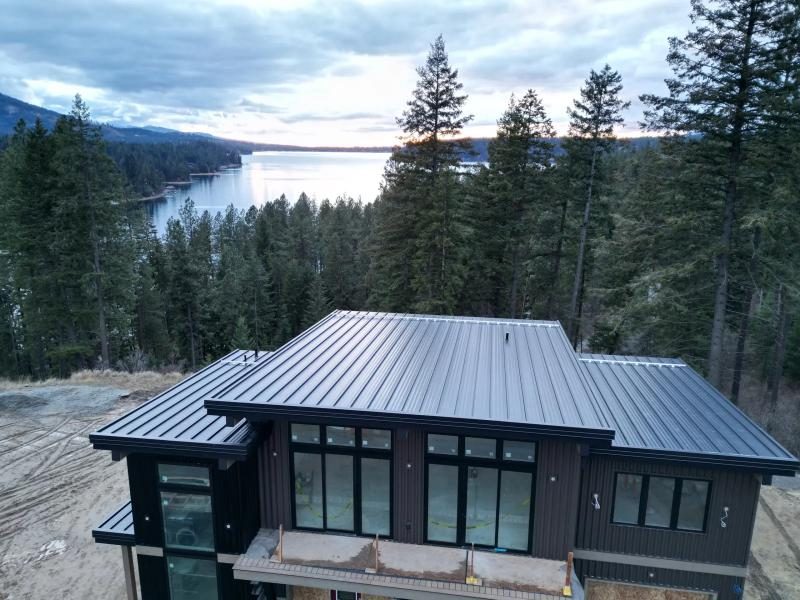 Drone view of a dark standing seam metal roof on a new home above a lake