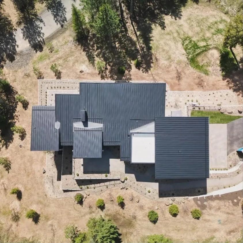 Overhead drone view of a dark standing seam metal roof with white TPO flat roof sections