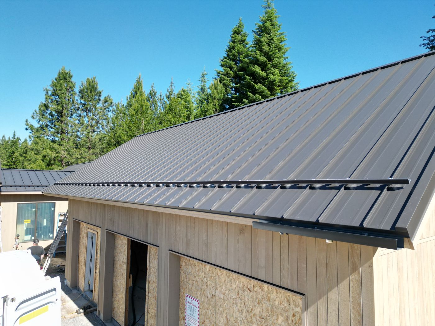 Snow retention bar installed along the eave of a dark standing seam roof over a garage